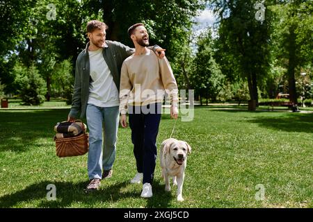 Ein glückliches bärtiges Schwulenpaar schlendert mit ihrem labrador Retriever durch einen grünen Park. Stockfoto