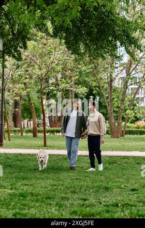 Ein bärtiges Schwulenpaar geht Hand in Hand durch einen grünen Park mit ihrem labrador Retriever. Stockfoto