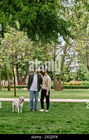 Ein bärtiges Schwulenpaar in lässiger Kleidung genießt einen sonnigen Nachmittag im Park mit seinem labrador Retriever. Stockfoto