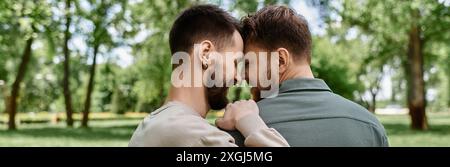 Zwei bärtige schwule Männer in lässiger Kleidung stehen in einem grünen Park nahe beieinander. Stockfoto