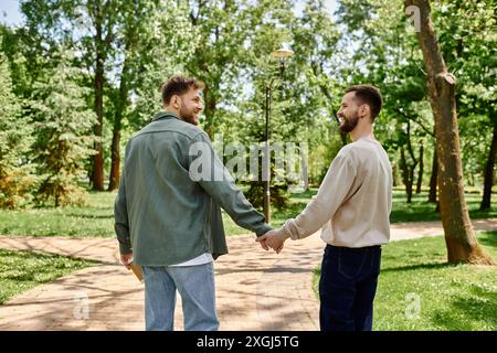 Ein schwules Paar mit Bärten geht an einem sonnigen Tag Hand in Hand durch einen Park. Stockfoto