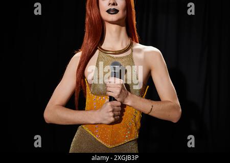 Eine Drag Queen in einem goldenen Outfit hält ein Mikrofon auf der Bühne. Stockfoto