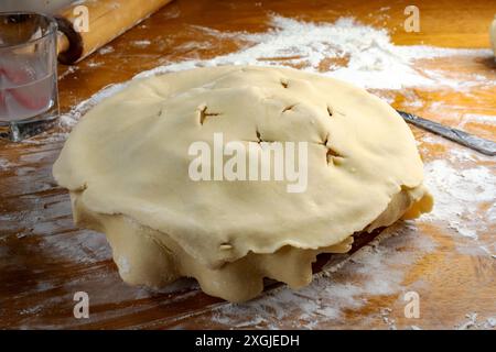 Torte machen: Oberste Kruste. Der Teig wird entfaltet, wobei die Kanten seitlich über dem vorbereiteten Apfelkuchen hängen. Stockfoto