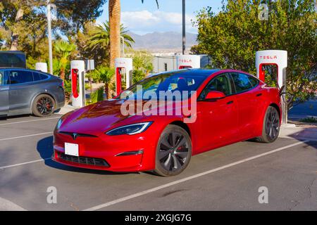 Los Angeles, Kalifornien - 15. April 2024: Red Tesla Model S lädt an einer Tesla Supercharger Station auf einem Parkplatz, der von Palmen umgeben ist Stockfoto