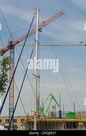 Baukräne und weißer Mast vor blauem Himmel Hintergrund. Hochwertige Fotos Stockfoto