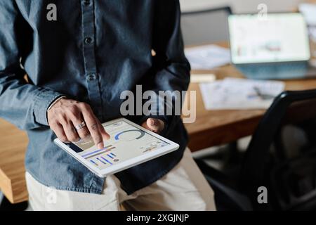 Mann zoomt bunte analytische Diagramme auf seinem Tablet, während er im Büro ist Stockfoto