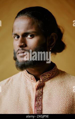 Ein hübsches, junges Indianermodell, das in einem Hemd mit Flachsmuster gekleidet ist und für Porträt sitzt, während man mit Schokoladenaugen in die Kamera blickt Stockfoto