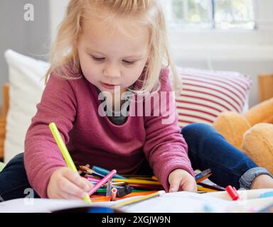 Kleines Mädchen, Färbung und Kleinkind mit Buch auf dem Bett zum Zeichnen oder zur Entwicklung der Kindheit zu Hause. Kleines Kind oder blonde weibliche Person von entzückend Stockfoto