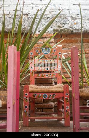 Dieses fesselnde Foto zeigt einen handbemalten Holzstuhl in einem leuchtenden Rosa, der mit komplizierten Blumenmustern verziert ist. Der Stuhl ist auf Agains gesetzt Stockfoto