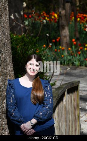 Besucher der Dixon Gallery and Gardens ruhen sich an einem Baumstamm und einer rustikalen Holzbrücke aus. Tulpen blühen hinter ihr. Sie lächelt und Stockfoto