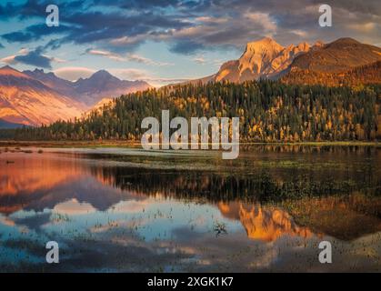 Dramatische Wolken und goldenes Licht reflektieren auf einem ruhigen Bergsee, umgeben von farbenfrohen Herbstwäldern Stockfoto
