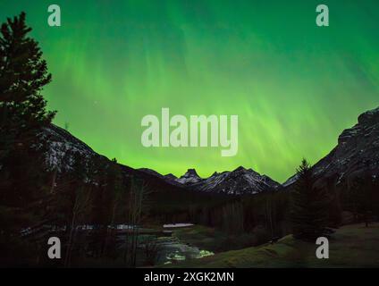 Die wunderschöne aurora Borealis beleuchtet den Nachthimmel mit leuchtenden Grüntönen über schneebedeckten Bergen Stockfoto