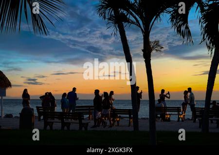 Die Leute versammeln sich bei Sonnenuntergang zu einer Strandparty unter den Palmen in der Karibik Stockfoto