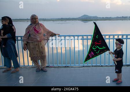 Srinagar, Indien. Juli 2024. Ein schiitischer muslimischer Junge aus Kaschmir hält eine islamische Flagge an der Uferstraße in Srinagar. Muharram ist der erste Monat des islamischen Kalenders. Es ist einer der heiligsten Monate im islamischen Kalender. Schiitische Muslime gedenken Muharram als einen Monat der Trauer zum Gedenken an das Martyrium des islamischen Propheten Muhammads Enkel Imam Hussain, der 680 n. Chr. auf Ashura (10. Tag Muharram) in der Schlacht von Karbala getötet wurde Stockfoto