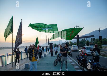 Srinagar, Indien. Juli 2024. Kaschmiri schiitische muslimische Männer schwenken islamische Fahnen, die an der Uferstraße in Srinagar stehen. Muharram ist der erste Monat des islamischen Kalenders. Es ist einer der heiligsten Monate im islamischen Kalender. Schiitische Muslime gedenken Muharram als einen Monat der Trauer zum Gedenken an das Martyrium des islamischen Propheten Muhammads Enkel Imam Hussain, der 680 n. Chr. auf Ashura (10. Tag Muharram) in der Schlacht von Karbala getötet wurde Stockfoto