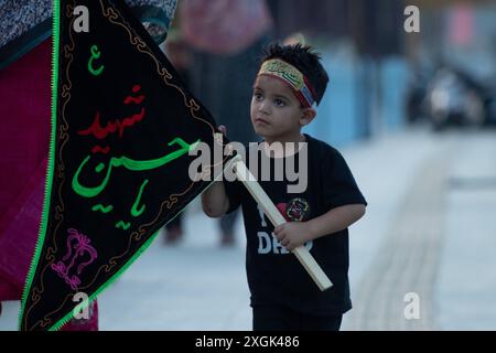 Srinagar, Indien. Juli 2024. Ein schiitisches muslimitisches Kind aus Kaschmir hält eine islamische Flagge an der Uferstraße in Srinagar. Muharram ist der erste Monat des islamischen Kalenders. Es ist einer der heiligsten Monate im islamischen Kalender. Schiitische Muslime gedenken Muharram als einen Monat der Trauer zum Gedenken an das Martyrium des islamischen Propheten Muhammads Enkel Imam Hussain, der 680 n. Chr. auf Ashura (10. Tag Muharram) in der Schlacht von Karbala getötet wurde Stockfoto