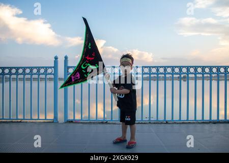 Srinagar, Indien. Juli 2024. Ein schiitisches muslimitisches Kind aus Kaschmir hält eine islamische Flagge an der Uferstraße in Srinagar. Muharram ist der erste Monat des islamischen Kalenders. Es ist einer der heiligsten Monate im islamischen Kalender. Schiitische Muslime gedenken Muharram als einen Monat der Trauer zum Gedenken an das Martyrium des islamischen Propheten Muhammads Enkel Imam Hussain, der 680 n. Chr. in der Schlacht von Karbala auf Ashura (10. Tag Muharram) getötet wurde (Foto: Faisal Bashir/SOPA Images/SIPA USA) Credit: SIPA USA/Alamy Live News Stockfoto