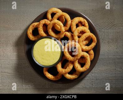 Teller mit gebratenen Zwiebelringen und Knoblauchsoße auf hölzernem Küchentisch Hintergrund, Blick von oben Stockfoto