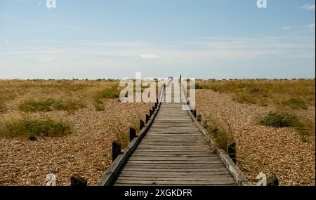 Holzbrettspaziergang über den Strand zum Meer in Dungeness, Kent Stockfoto