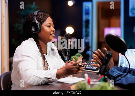 Eine weibliche Radiosenderin führt Gespräche mit einer Person, nimmt mit Audiogeräten auf, um das Publikum live zu hören. Influencer, der gerne mit Journalisten chatten und Diskussionen über Rundfunk sendet. Stockfoto