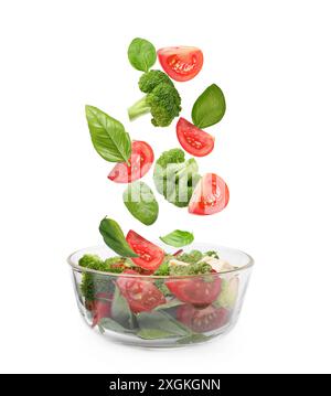 Frisches Gemüse für Salat, das in die Schüssel fällt, auf weißem Hintergrund Stockfoto