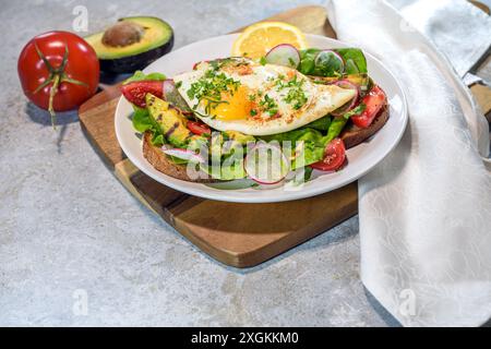 Geröstetes Brot mit gegrillter Avocado, Spiegelei, Salat, Tomaten, Rettich und Kräutergarnitur auf einem Teller und einem hölzernen Küchenbrett, gesunde Mahlzeit für Brot Stockfoto