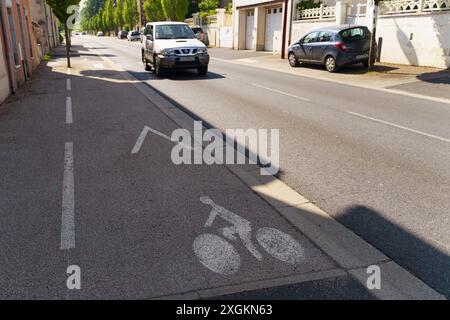 Langeac, Frankreich - 28. Mai 2023: Ein bemalter Fahrradweg mit einem weißen Fahrradsymbol in einer ruhigen Straße in Langeac, Frankreich. Die Straße ist von Bäumen umgeben Stockfoto
