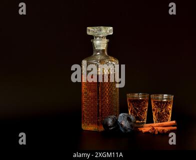 Pflaumenlikör mit Gewürzen auf schwarzem Hintergrund, hausgemachter Alkohol in Kristallgläsern, Zimt und Anis. Nahaufnahme. Stockfoto