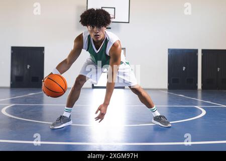 Ein junger birassischer Mann spielt Basketball in Innenräumen und zeigt seinen sportlichen Lebensstil. Seine sportliche Haltung spiegelt seinen Fokus und sein Können auf dem Platz wider. Stockfoto