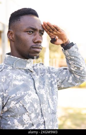 Fokussierter afroamerikanischer Soldat in Uniform, der draußen grüßt. Militärdienst, Armee, Arbeit, Aufmerksamkeit und Pflicht, unverändert. Stockfoto