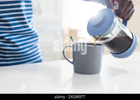 Mitte des afroamerikanischen Mannes, der Kaffee aus dem Café in der Küche gießt. Erfrischung, Morgen, Hausleben und Lebensstil, unverändert. Stockfoto