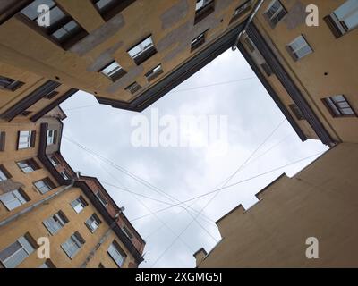 Blick von einem städtischen Innenhof, umgeben von Gebäuden mit bewölktem Himmel. Das Bild erfasst Architektur und einen offenen Himmel. Stockfoto