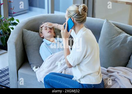 Telefonanruf, Kind und Mutter auf Fieber mit Grippe, Erkältung oder Allergie auf Sofa zu Hause. Krank, medizinischer Notfall und Mutter fühlen Kopf des Kindes für hoch Stockfoto