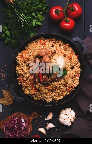 Usbekische Pilaw, gedünsteter Reis mit Fleisch, in einem gusseisernen Kessel, auf einem dunkelgrauen Holztisch, Blick von oben, keine Leute, getönt Stockfoto