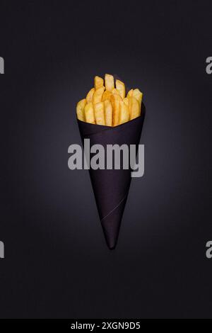 Pommes Frites, in schwarzer Papierverpackung, auf schwarzem Hintergrund, Nahaufnahme, selektiver Fokus Stockfoto