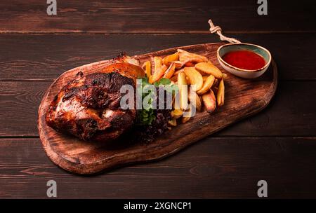 Schweinehaxe, in Sojahonig-Sauce, mit gebratenen Kartoffeln, auf Holzschneidebrett, hausgemacht, keine Leute Stockfoto