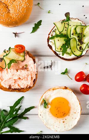 Auswahl an Sandwiches, Weißbrot, Spiegelei, Frischkäse und Gurke, Capelin Kaviar, Sesambrötchen, Frühstück, auf einem weißen Tisch, vertikal, nein Stockfoto