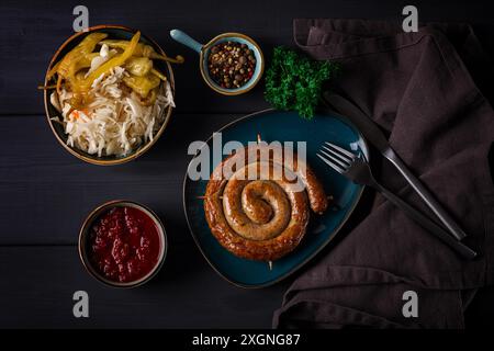 Traditionelles deutsches Gericht, gebratene Spiralwurst, mit Sauerkraut, mit roter Sauce, auf dunkelgrauem Holzhintergrund, Blick von oben, horizontal, keine Leute Stockfoto