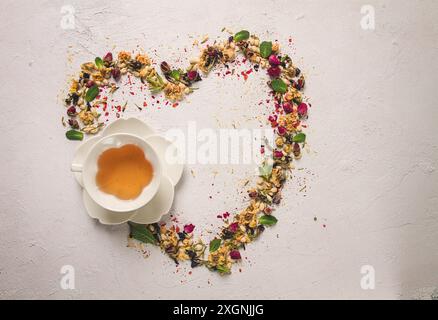 Tee-Set, Herzform, mit einer Tasse, Draufsicht, auf weißem Hintergrund, Rosenknospen, Jasmin, Blau, Chrysantheme, Minzblätter Stockfoto