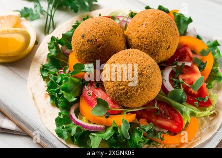 Tortillas, eingewickelte Falafelbällchen, mit frischem Gemüse, vegetarische gesunde Lebensmittel, auf einem hölzernen weißen Hintergrund, keine Menschen, selektiver Fokus Stockfoto