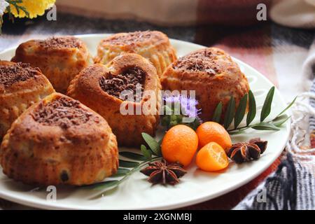 Herzförmige Kuchen und Muffins auf einem Teller mit Kumquats, Blumen und Sternanis auf einem karierten Tuch schaffen eine gemütliche und rustikale Atmosphäre Stockfoto