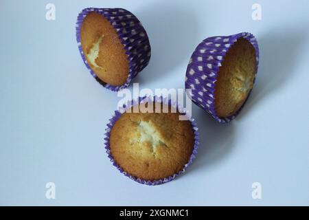 Drei Muffins in lila Polka Dot Liner auf einer weißen Oberfläche Stockfoto