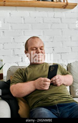 Ein Mann mit Inklusivität sitzt lässig gekleidet auf einer Couch und blättert mit einem Lächeln im Gesicht durch sein Handy. Stockfoto