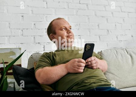 Ein Mann mit Inklusivität entspannt sich auf einer Couch in seinem Haus und hält ein Smartphone. Stockfoto