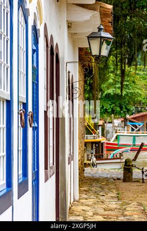 Hausfassaden im Kolonialstil mit alten Metalllaternen und Booten im Hintergrund in der historischen Stadt Paraty, Rio de Janeiro, Brasilien Stockfoto