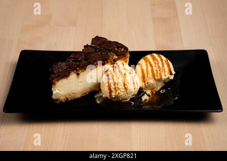 Ein köstlicher Dessertteller mit einer Scheibe Käsekuchen und Schaufeln Vanilleeis auf Holztisch Stockfoto