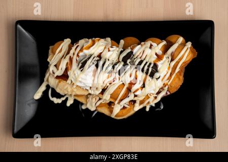 Ein Blick von oben auf eine köstliche Waffel mit Eiscreme, Schlagsahne und Schokoladensirup auf schwarzem Teller Stockfoto
