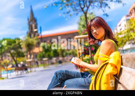 Asiatische coole junge Frau, die an einem sonnigen Tag auf einer Bank in der Stadt sitzt Stockfoto