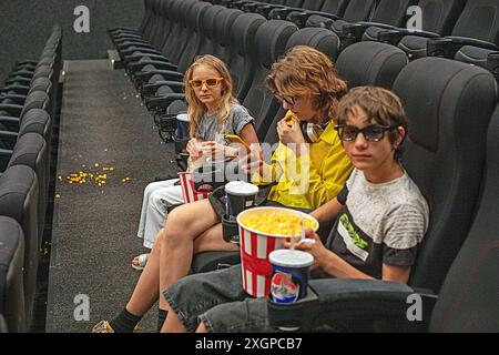 Kinder sitzen in der Kinohalle mit einer 3D-Brille mit Popcorn und einem Drink, bevor sie sich anschauen. Familienwochenende Stockfoto