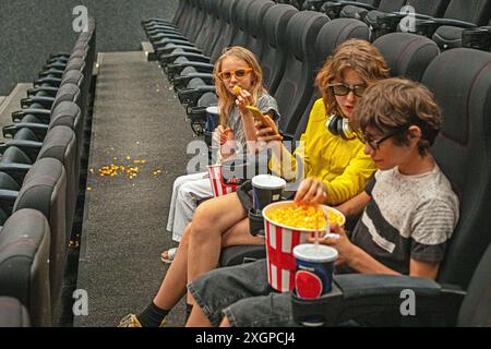 Kinder sitzen in der Kinohalle mit einer 3D-Brille mit Popcorn und einem Drink, bevor sie sich anschauen. Familienwochenende Stockfoto